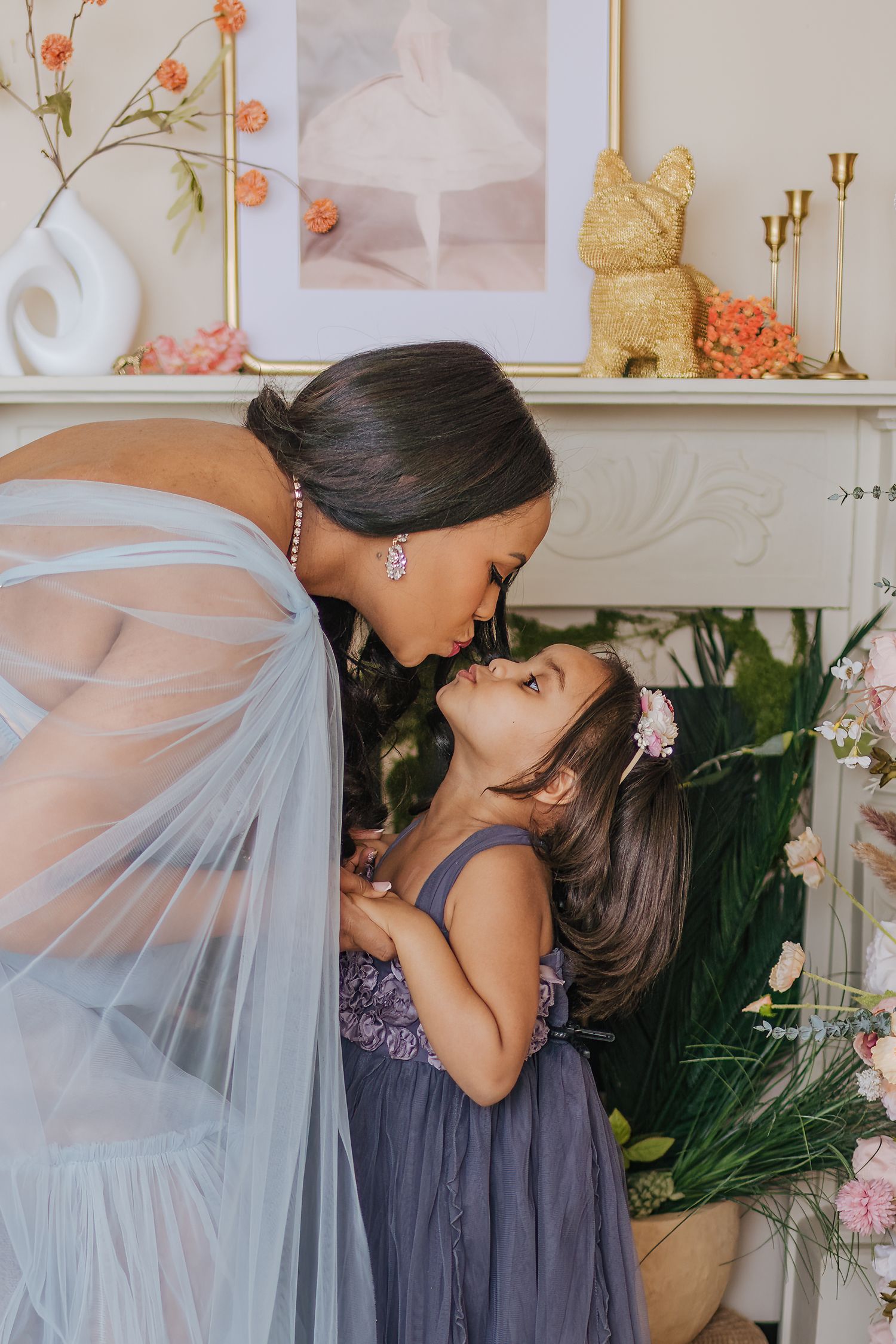 Tender moment between parent and child wearing elegant dresses amidst floral decor.