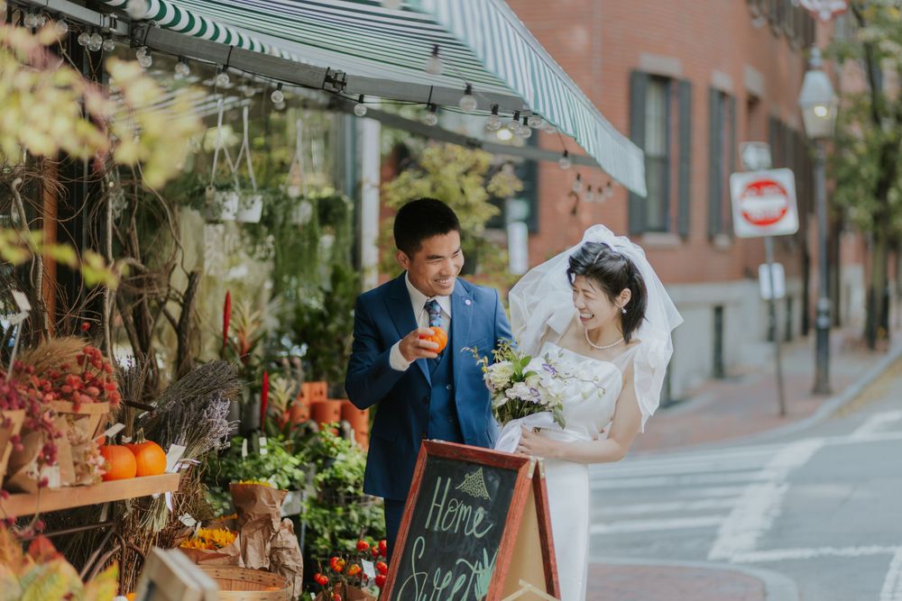 Newlyweds admiring flowers at a sidewalk florist shop with a chalkboard sign.