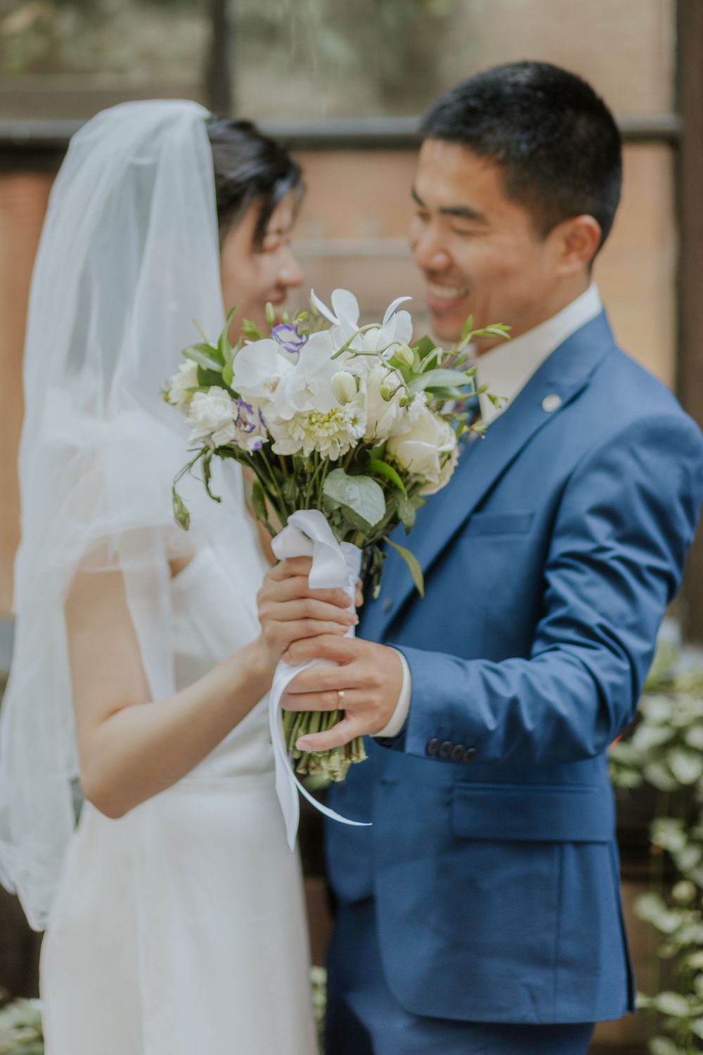 A tender moment between newlyweds as they hold a white floral bouquet together.