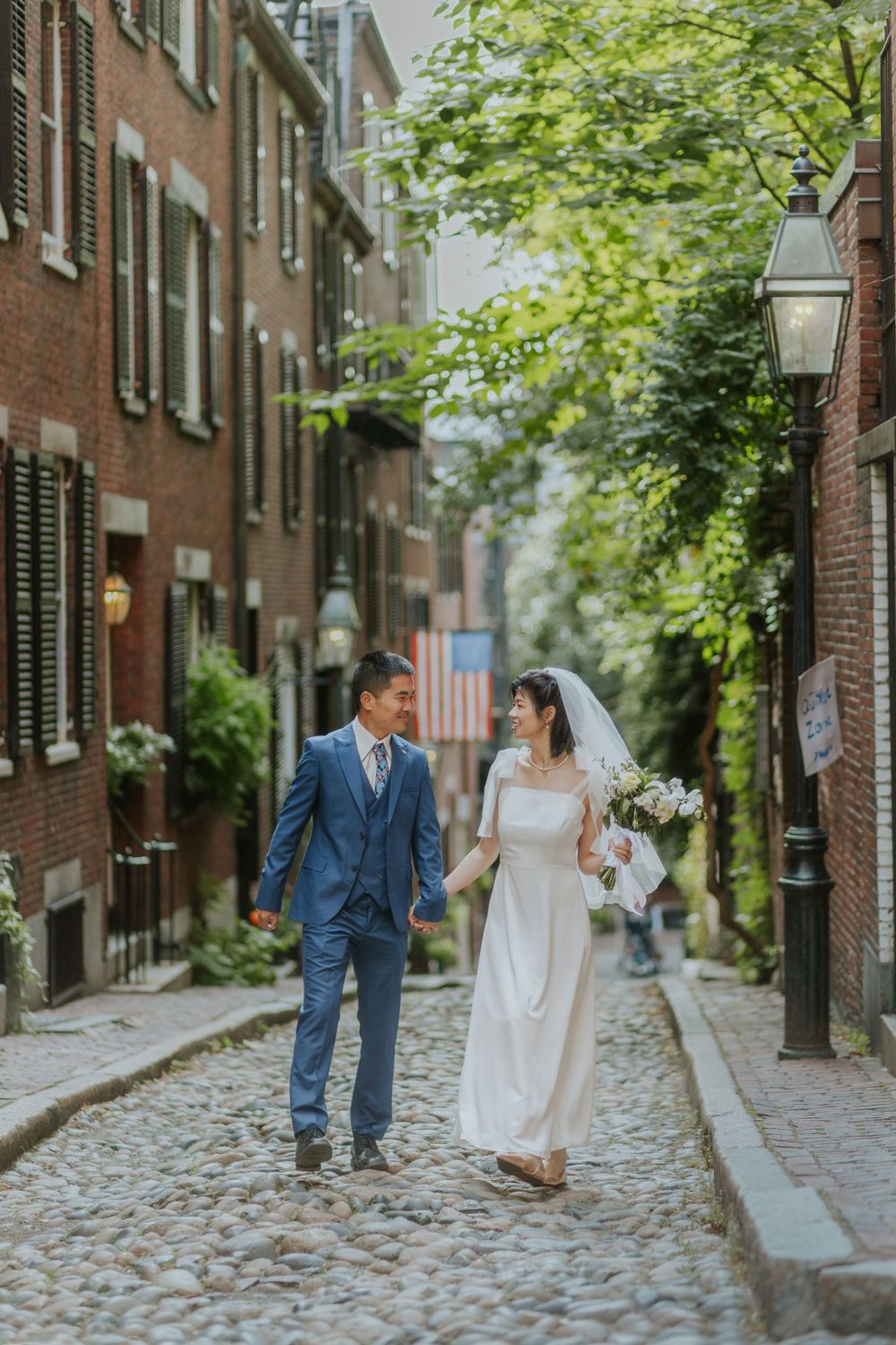 Newlyweds walking along a charming cobblestone street lined with historic brick buildings.