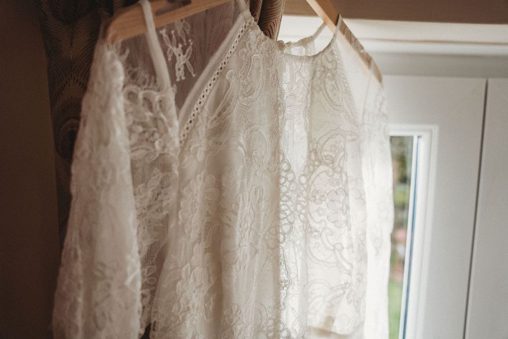 Vintage-style lace wedding dress hanging by window in natural light.