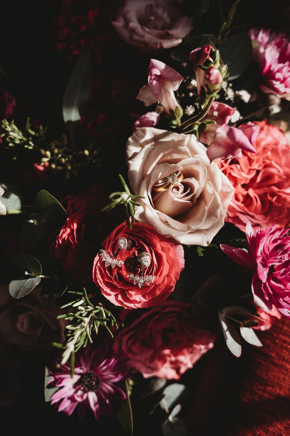 Romantic floral arrangement featuring pink and red roses with delicate greenery in moody lighting.