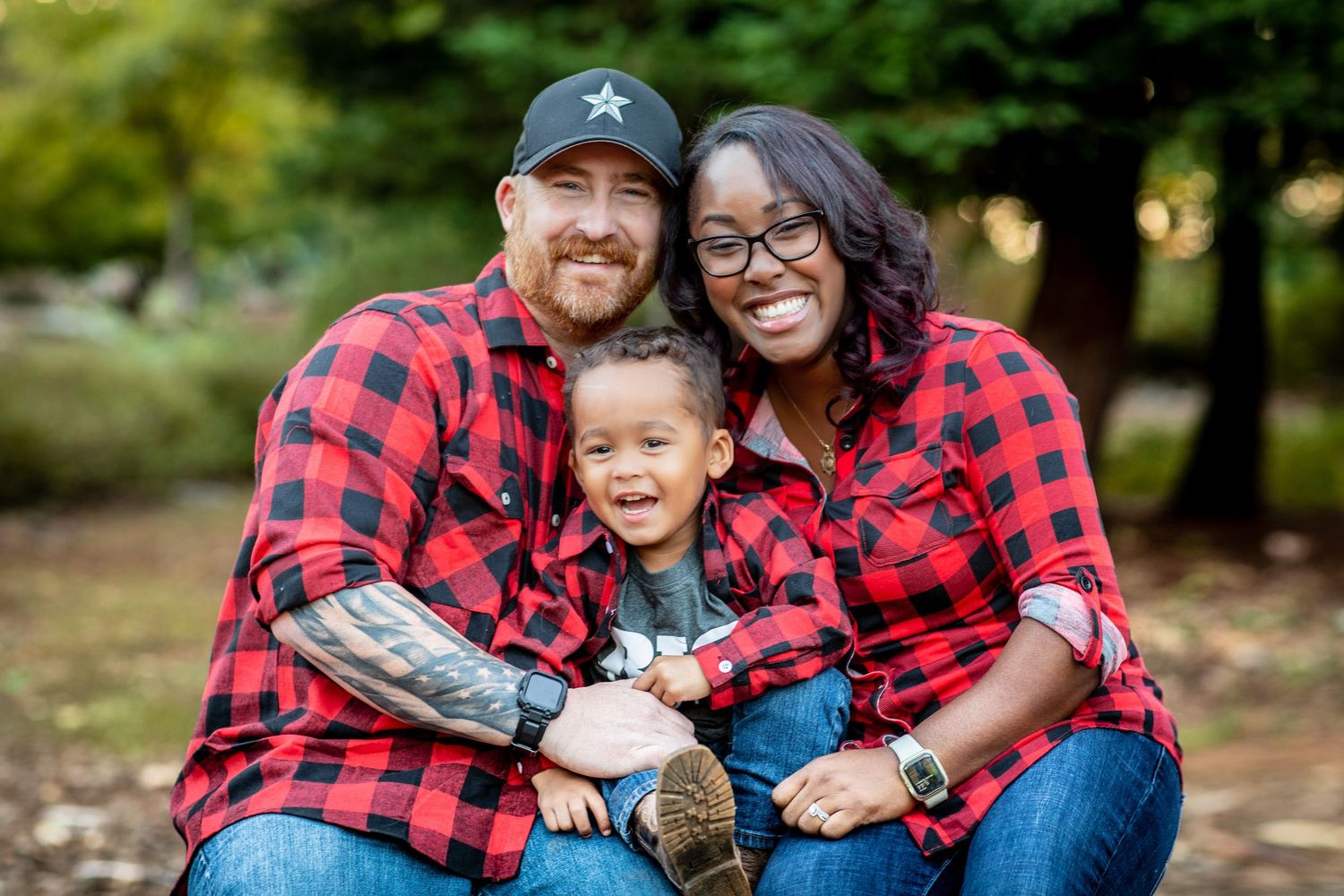 A family wearing matching red buffalo plaid shirts poses together outdoors for a fall photo session.