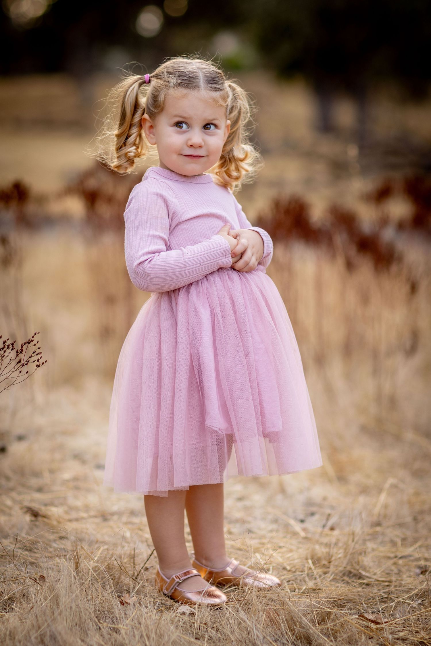 A small child in a pink tulle dress plays in a golden field during autumn.