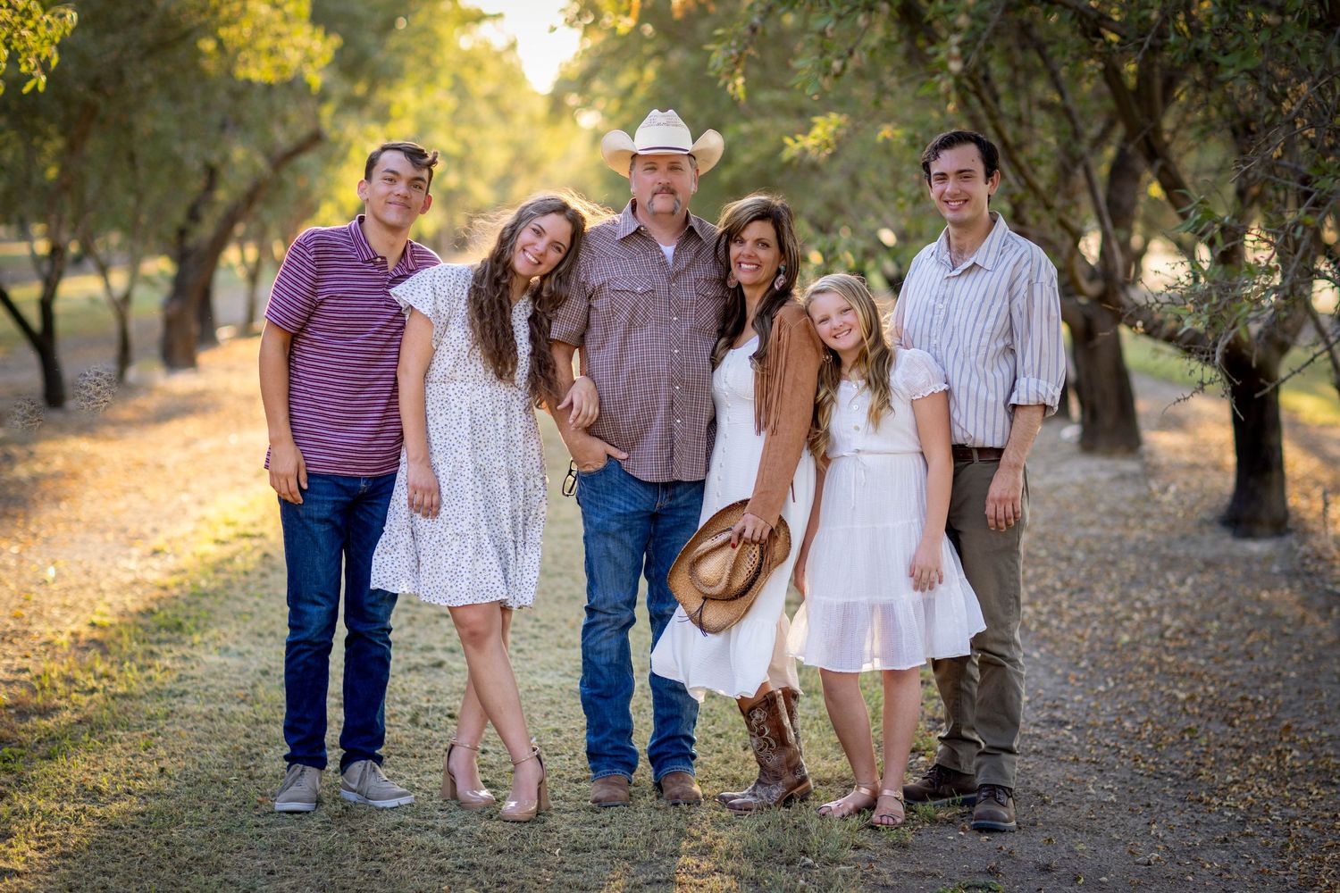 A group poses together on a tree-lined path during golden hour in casual attire.