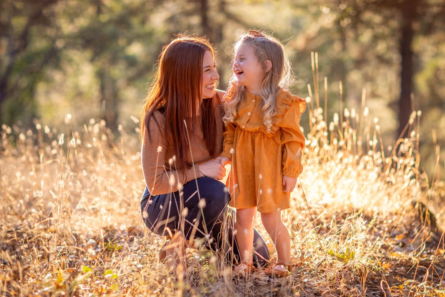 Two people sitting in a golden sunlit meadow with tall grass during sunset creating a warm, intimate atmosphere.