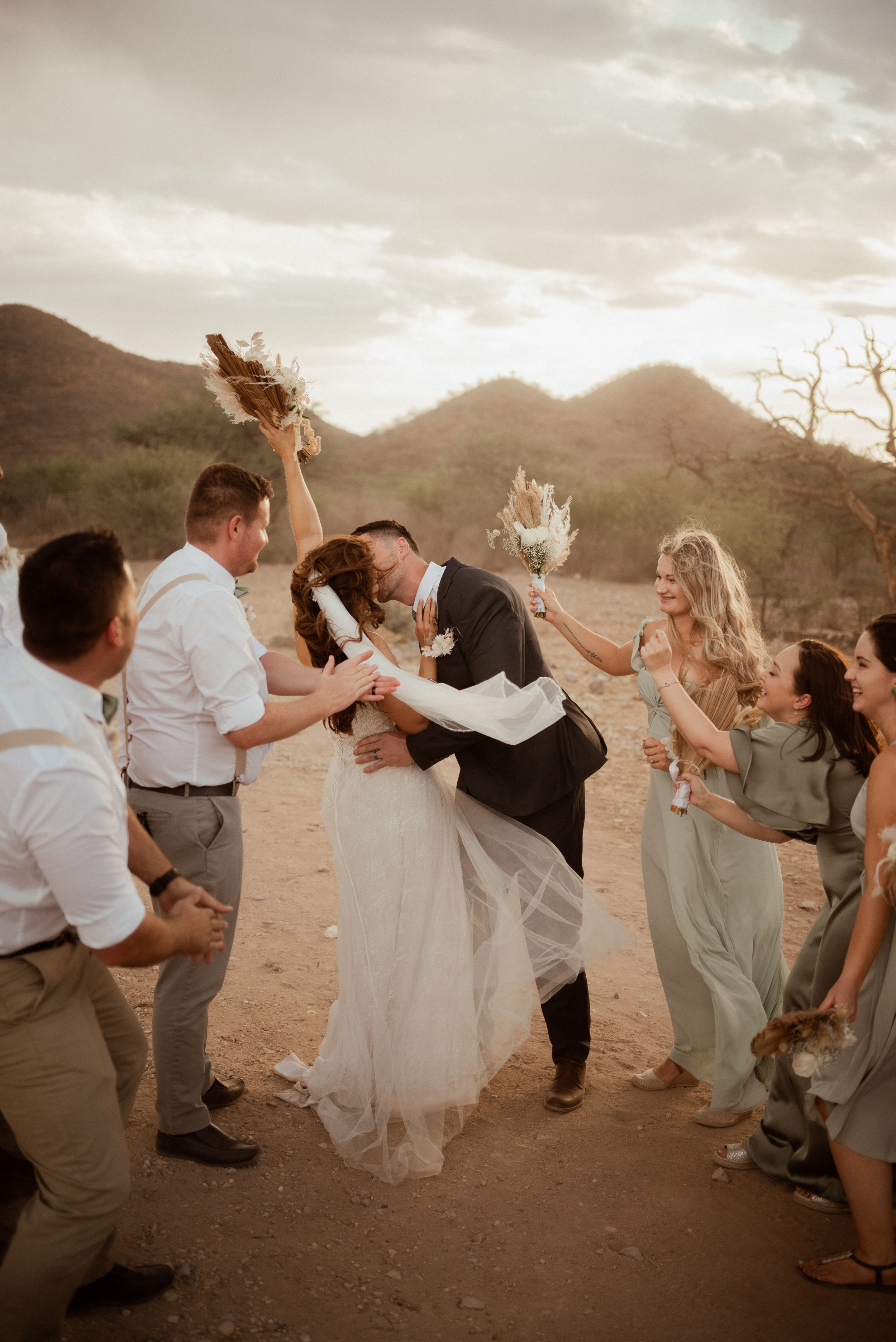 Wedding party celebrates joyfully on a mountain path during golden hour celebrations.
