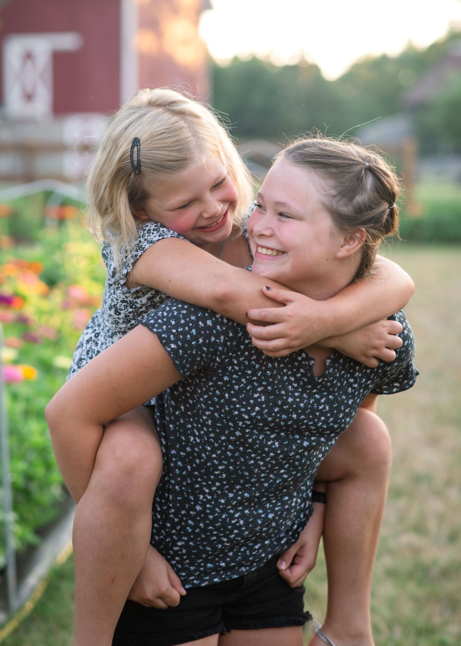 Two people share a playful piggyback ride in a garden at sunset.