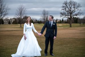 Wedding couple holding hands in an open field under dramatic cloudy sky.
