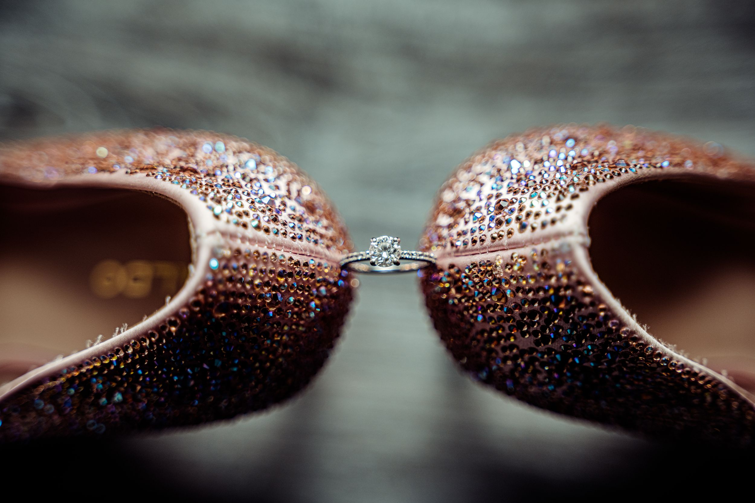 Sparkling wedding ring nestled between two rose gold glittery bridal shoes.