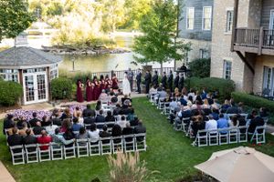 Aerial view of outdoor wedding ceremony with guests seated on white chairs by a waterfront venue.