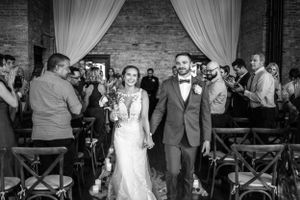 Wedding celebration exit through venue with draped brick walls and wooden chairs.
