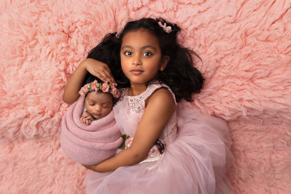 Two figures in pink tulle dresses posing against textured pink backdrop.