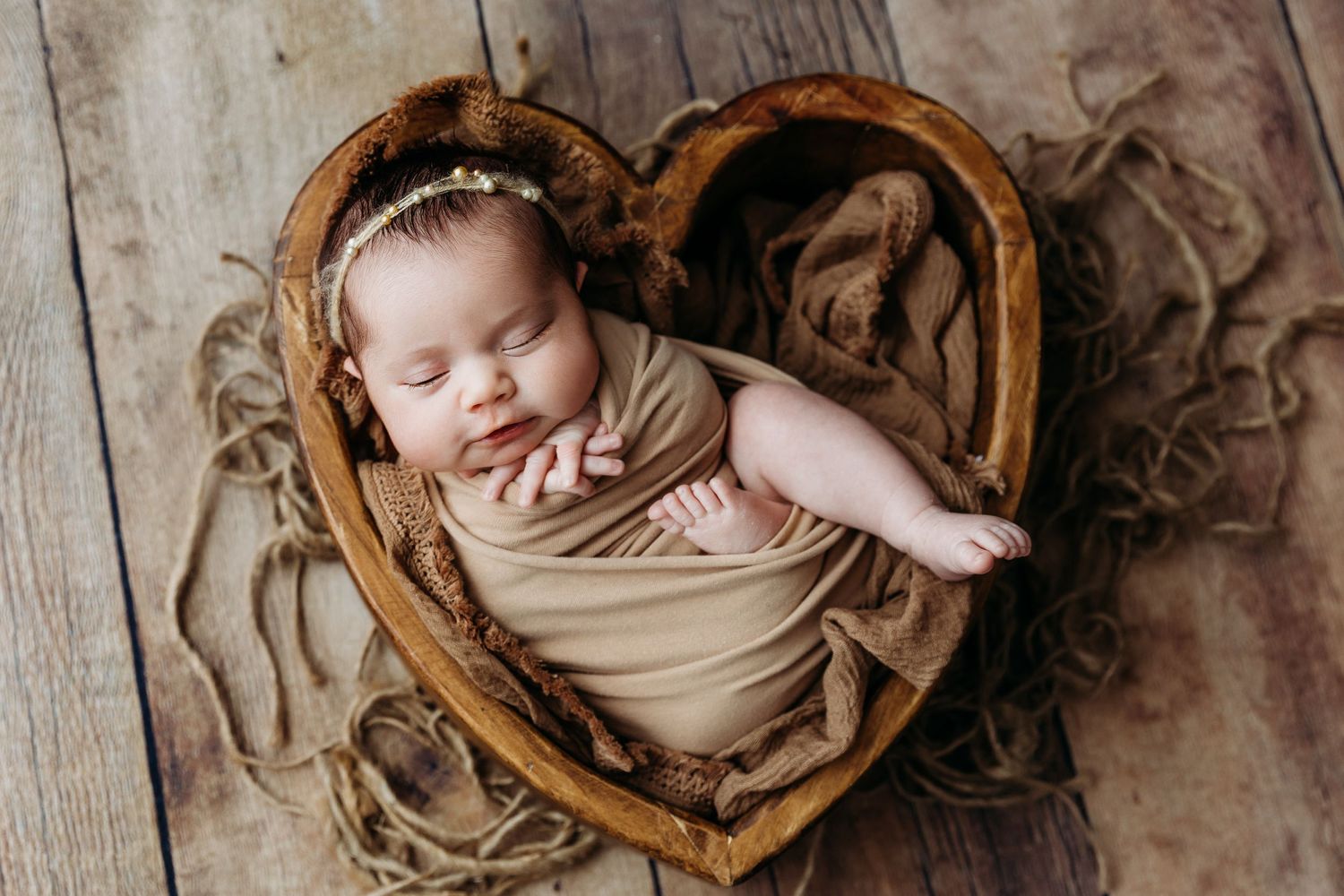 Newborn photography session with baby wrapped in neutral fabric on rustic wooden backdrop.