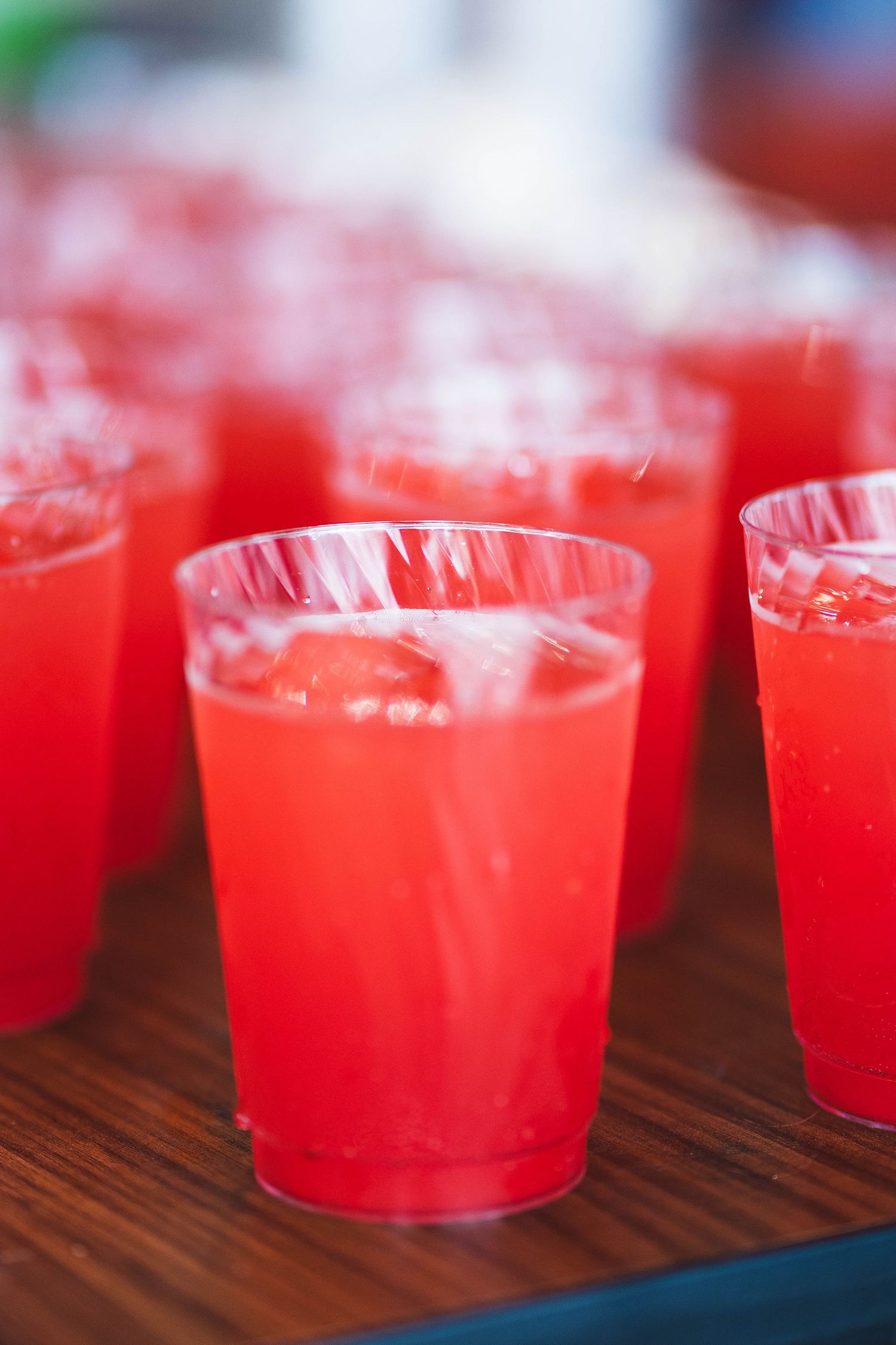 Multiple glasses of bright red cocktails lined up on a wooden surface.