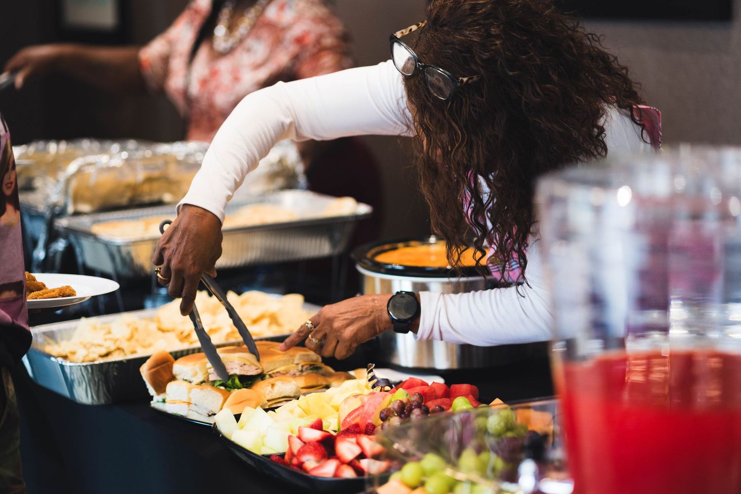 People serving themselves at a buffet table with various food dishes and drinks.