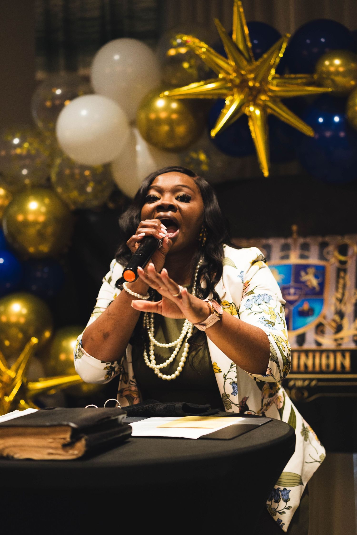 Performer singing passionately at an event with gold balloons and star decorations in the background.