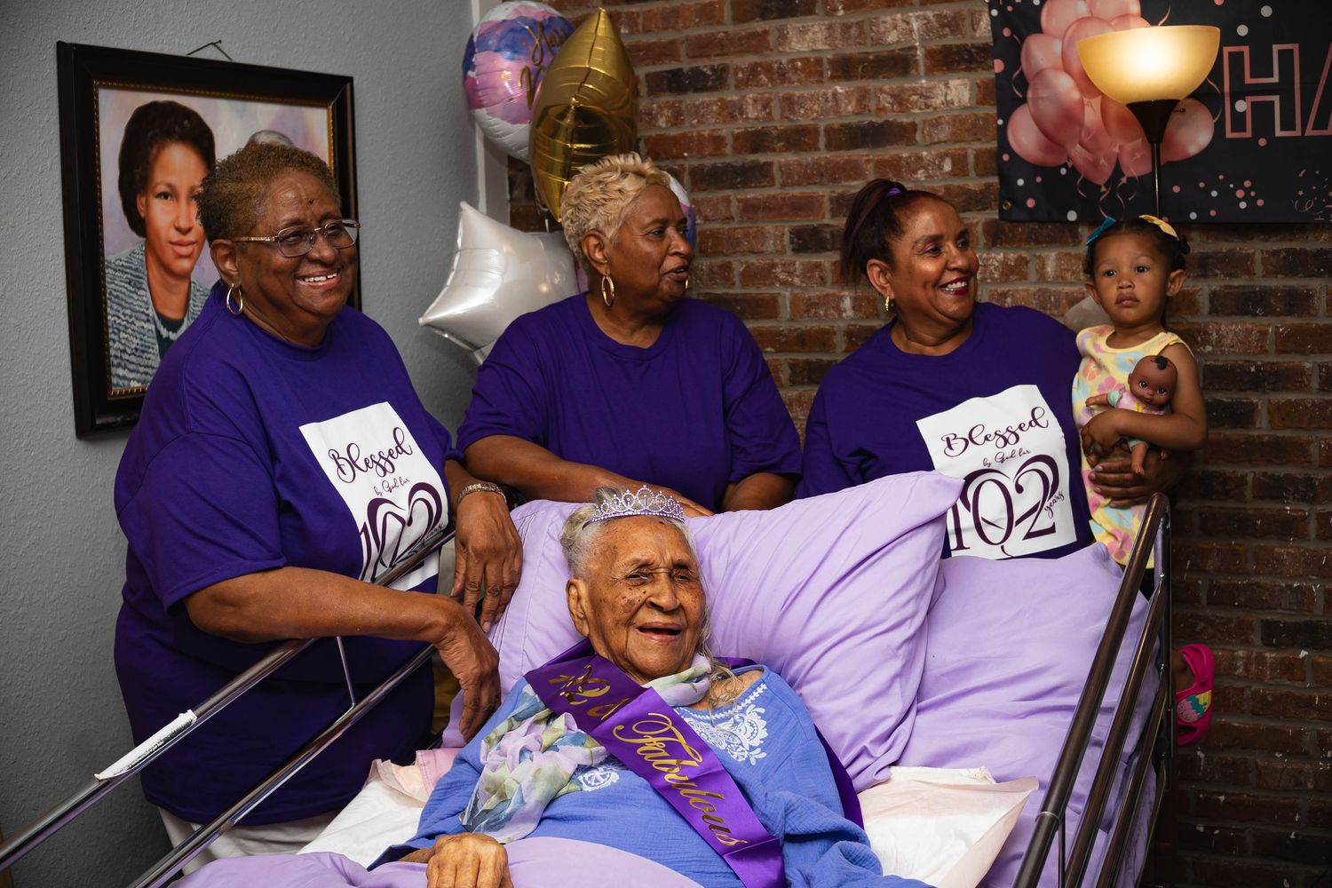 A group celebration in a room with brick walls, featuring matching purple shirts and balloons.
