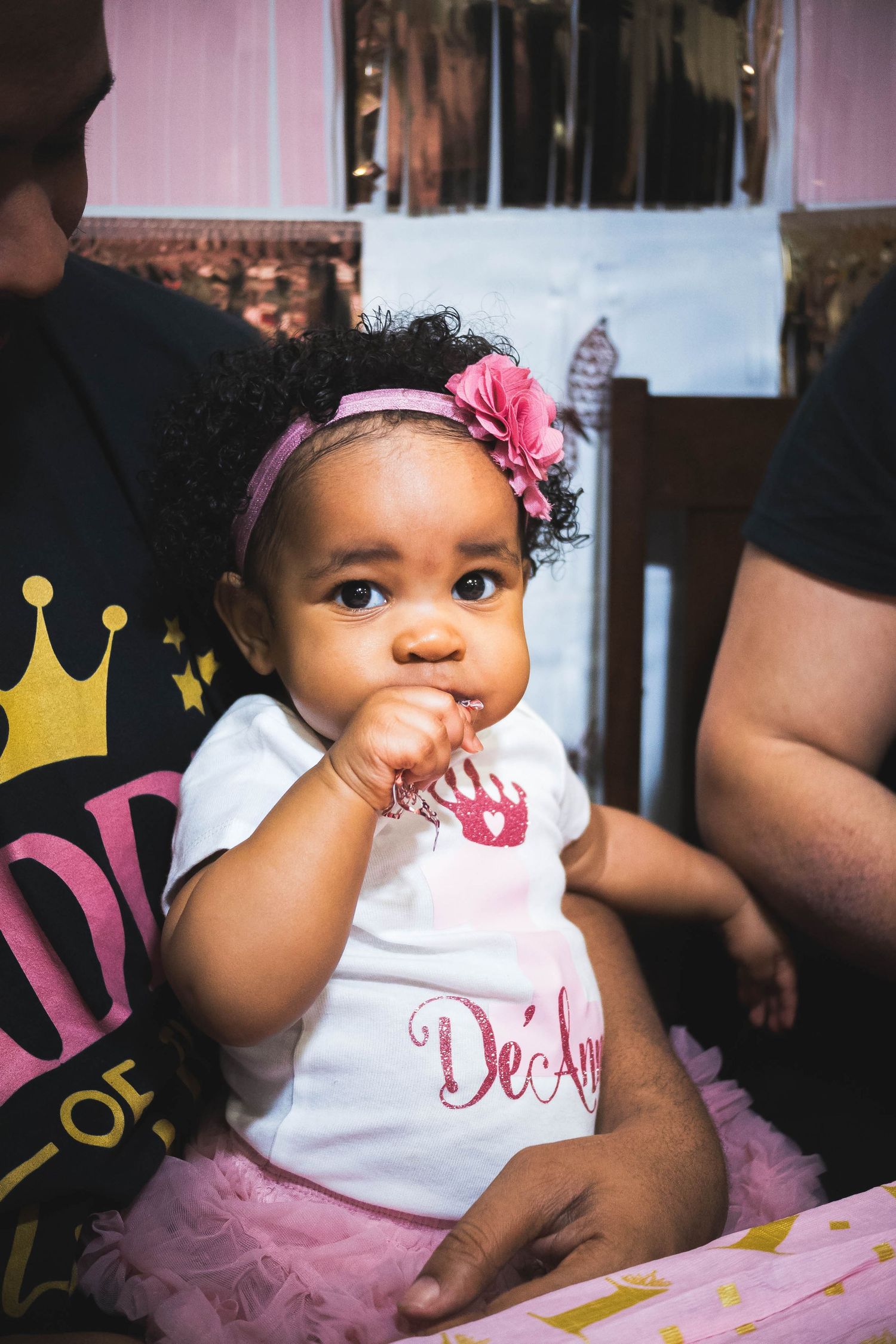 A baby in a tutu and floral headband sitting with a birthday cake.