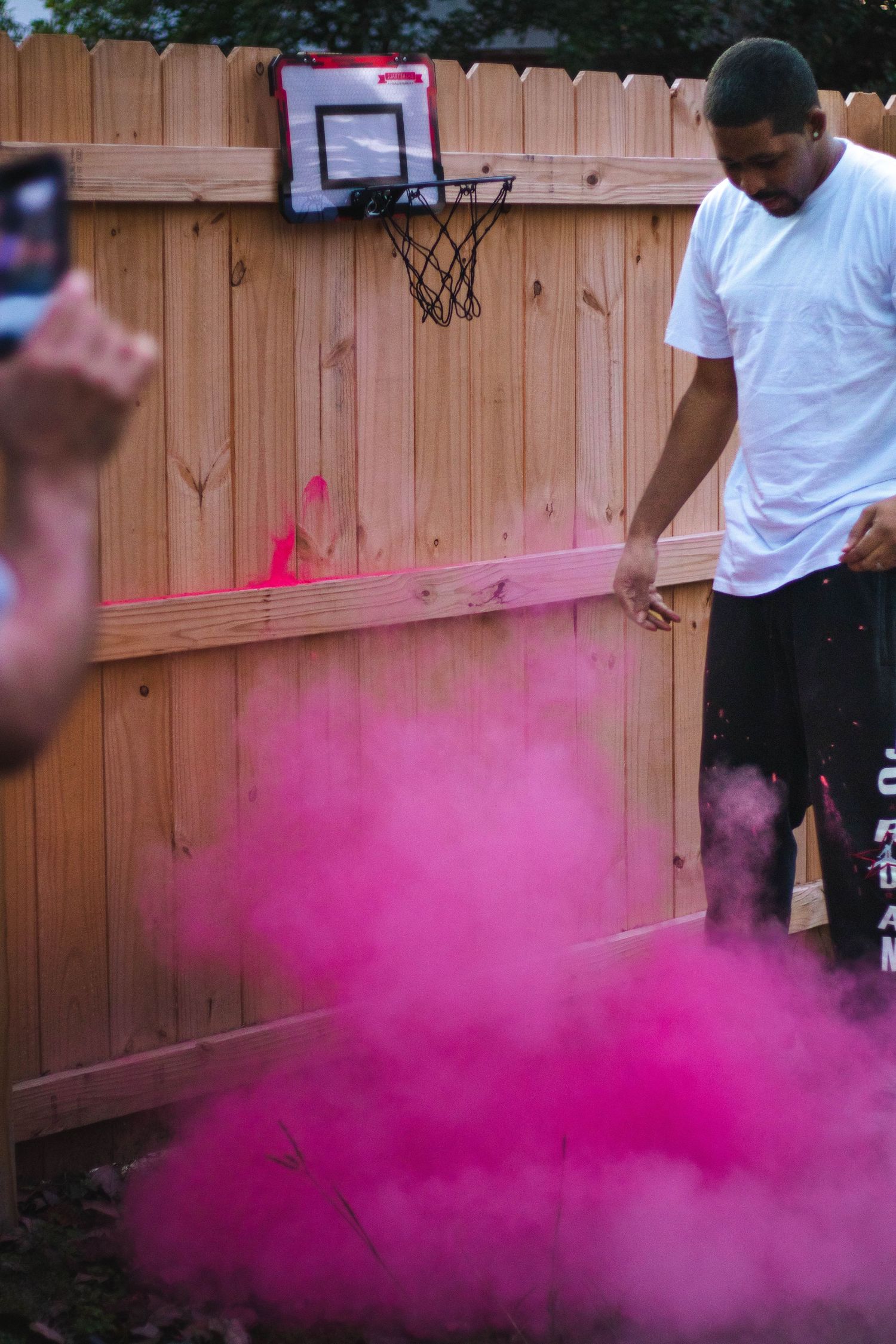 Pink smoke effect in backyard with basketball hoop mounted on wooden fence.