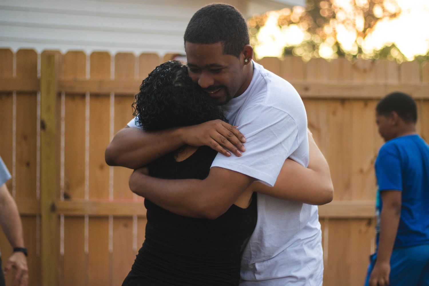 Emotional embrace between two people in backyard setting at sunset.