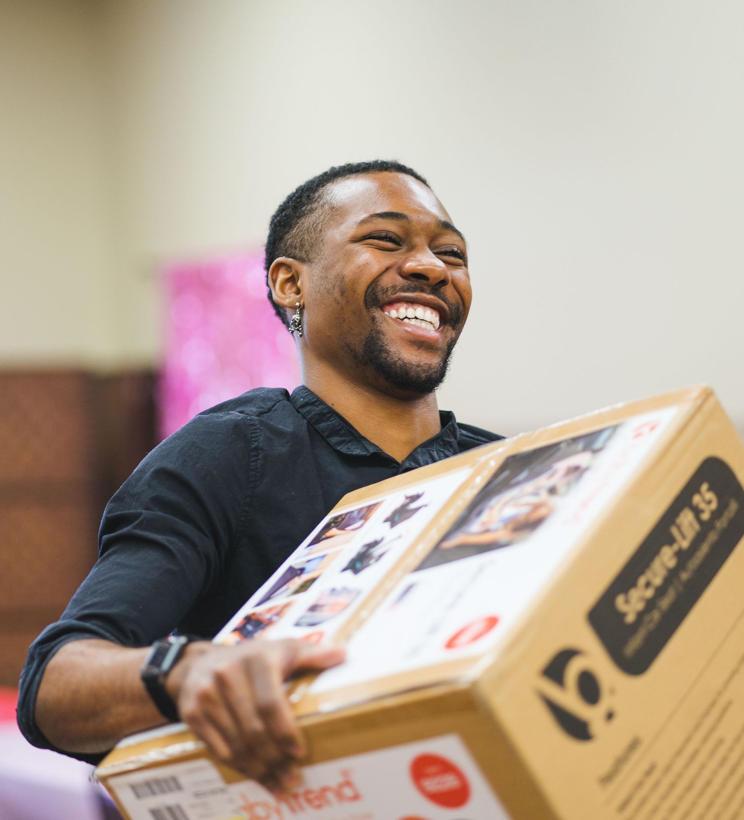 Person smiling while holding a cardboard box during delivery or unboxing.