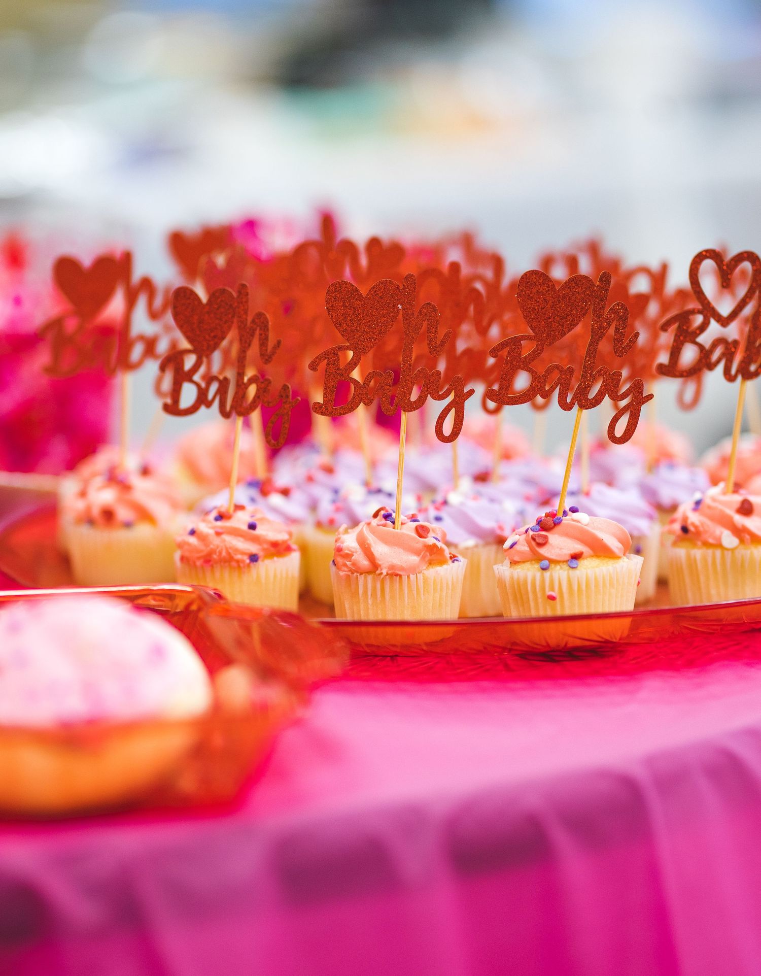 Pink cupcakes decorated with red glittery heart-shaped toppers that say Baby on them.