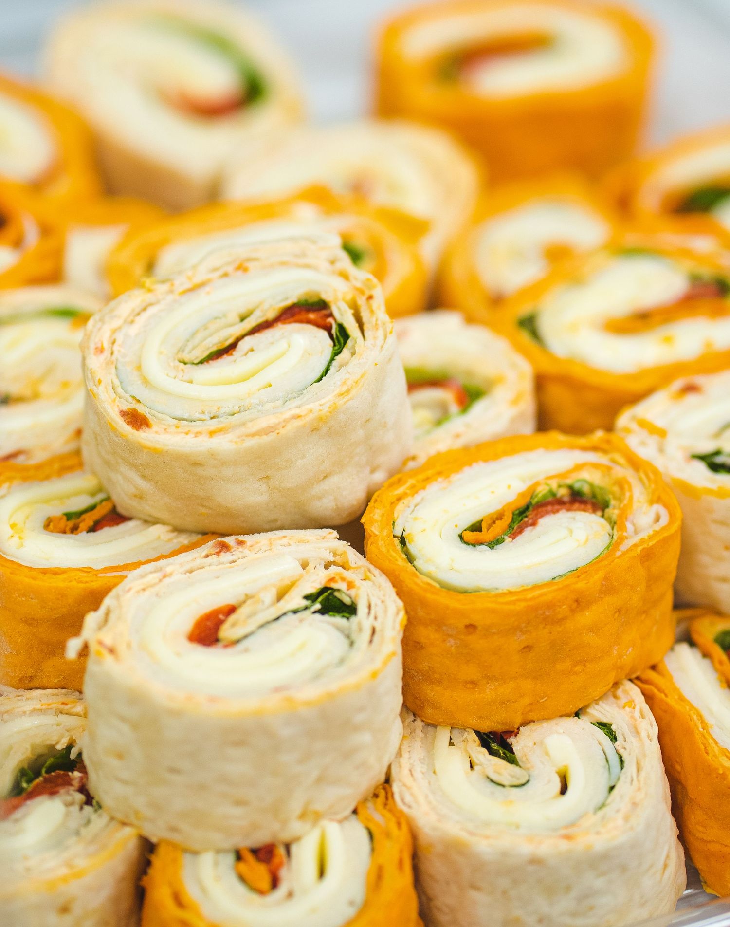 Colorful pinwheel sandwich rolls arranged in rows featuring orange and white tortillas with fillings.