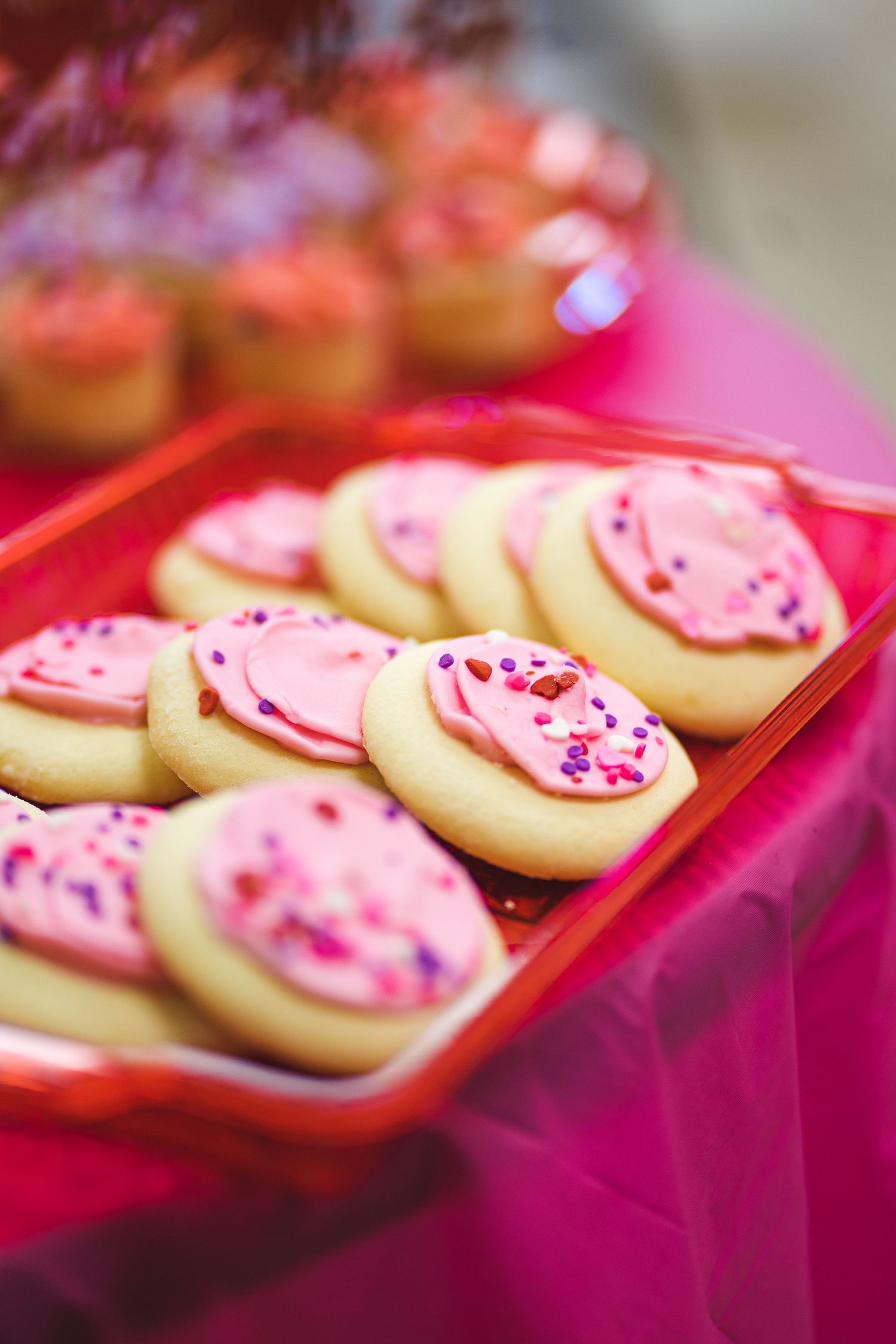 Pink frosted sugar cookies with sprinkles displayed on red serving tray.