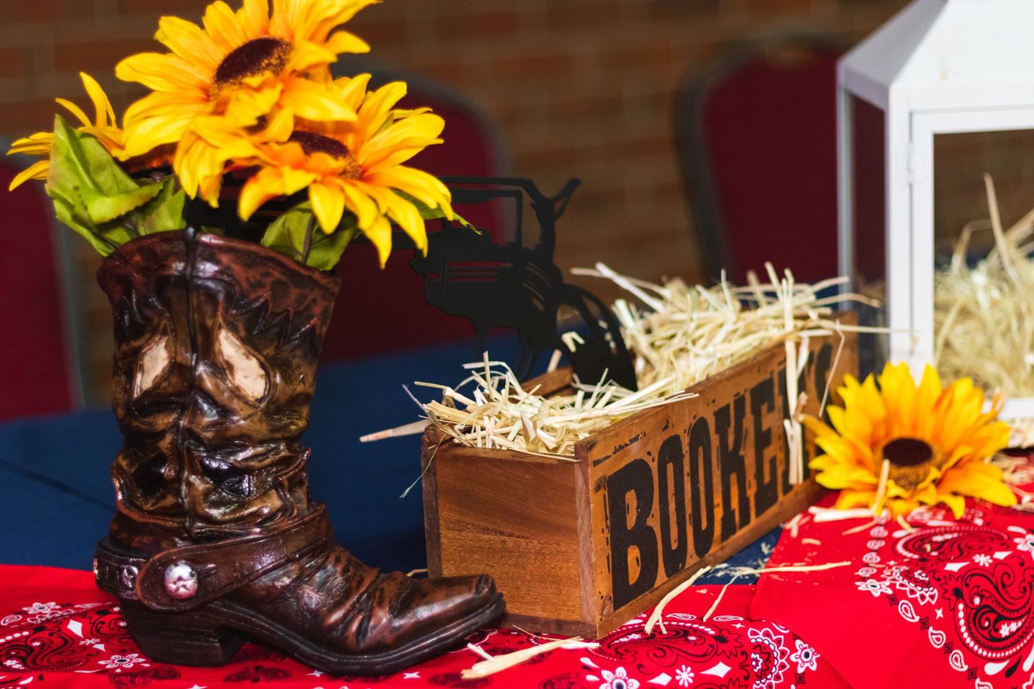 Rustic party decor with a cowboy boot vase holding sunflowers next to hay bales and wooden boxes.