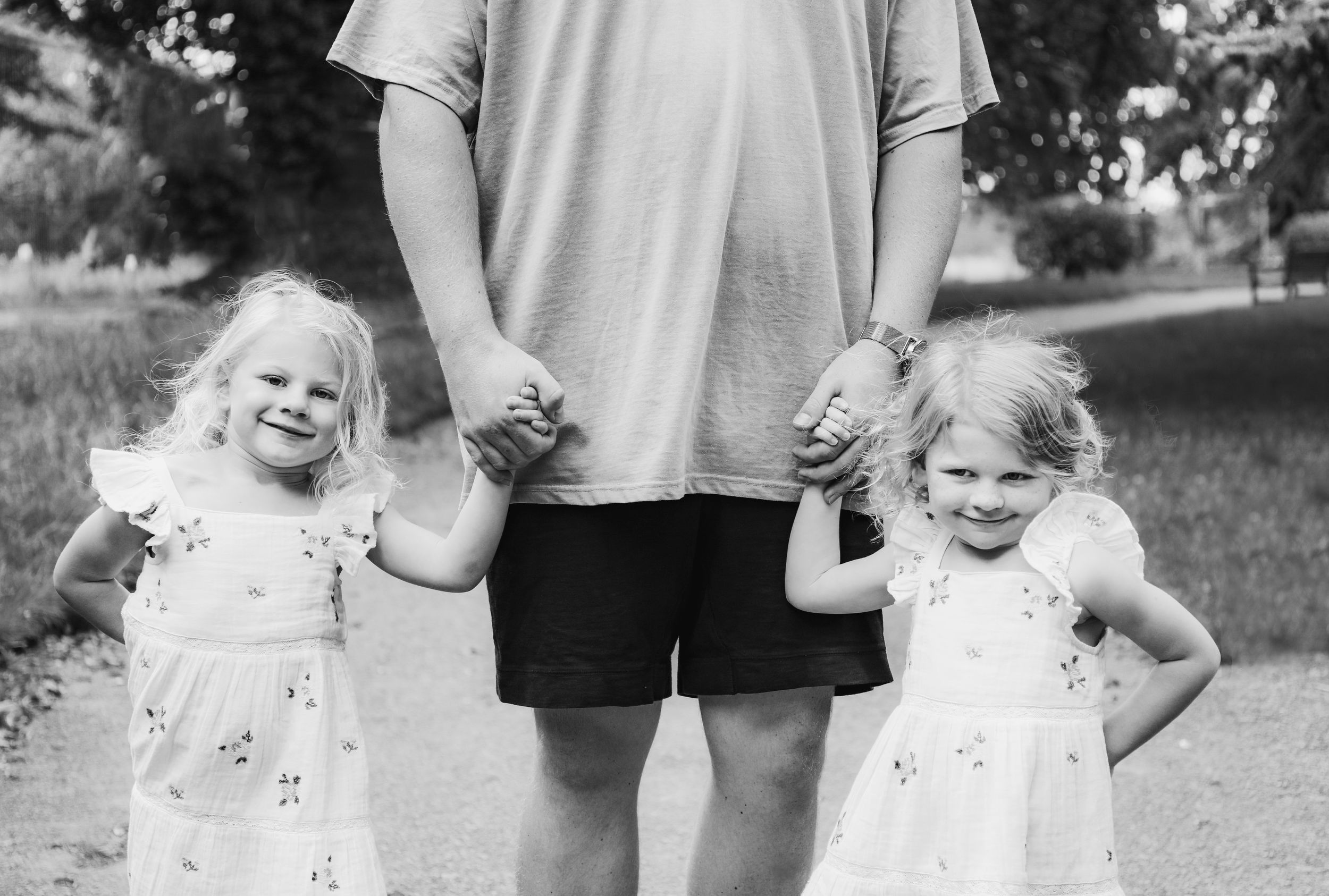 Black and white photo of two children holding hands with adult figure in outdoor setting.