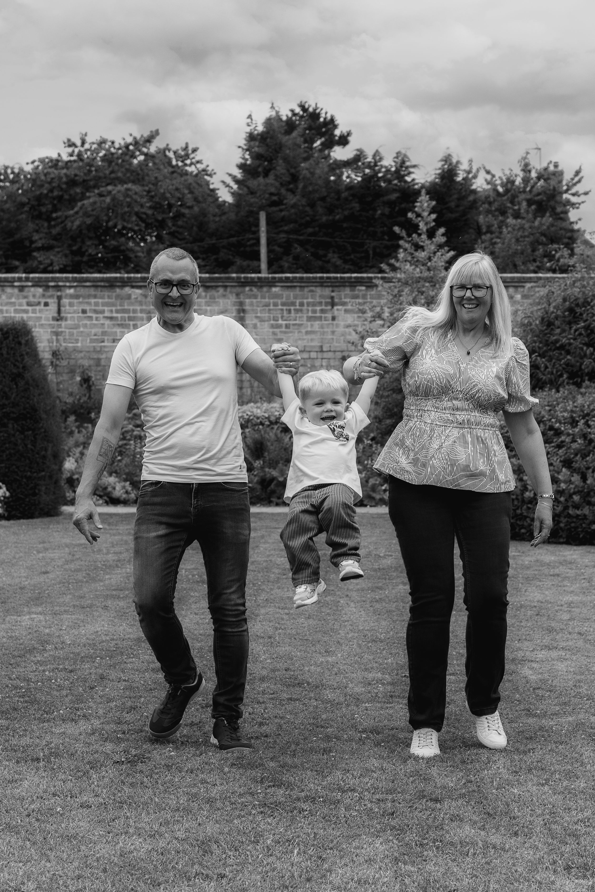 Black and white photo of grandparents lifting a smiling toddler during outdoor family photoshoot Nottingham