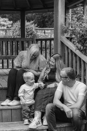 Black and white photo of a family with a toddler sitting on wooden porch steps sharing a joyful moment together Nottingham family photoshoot