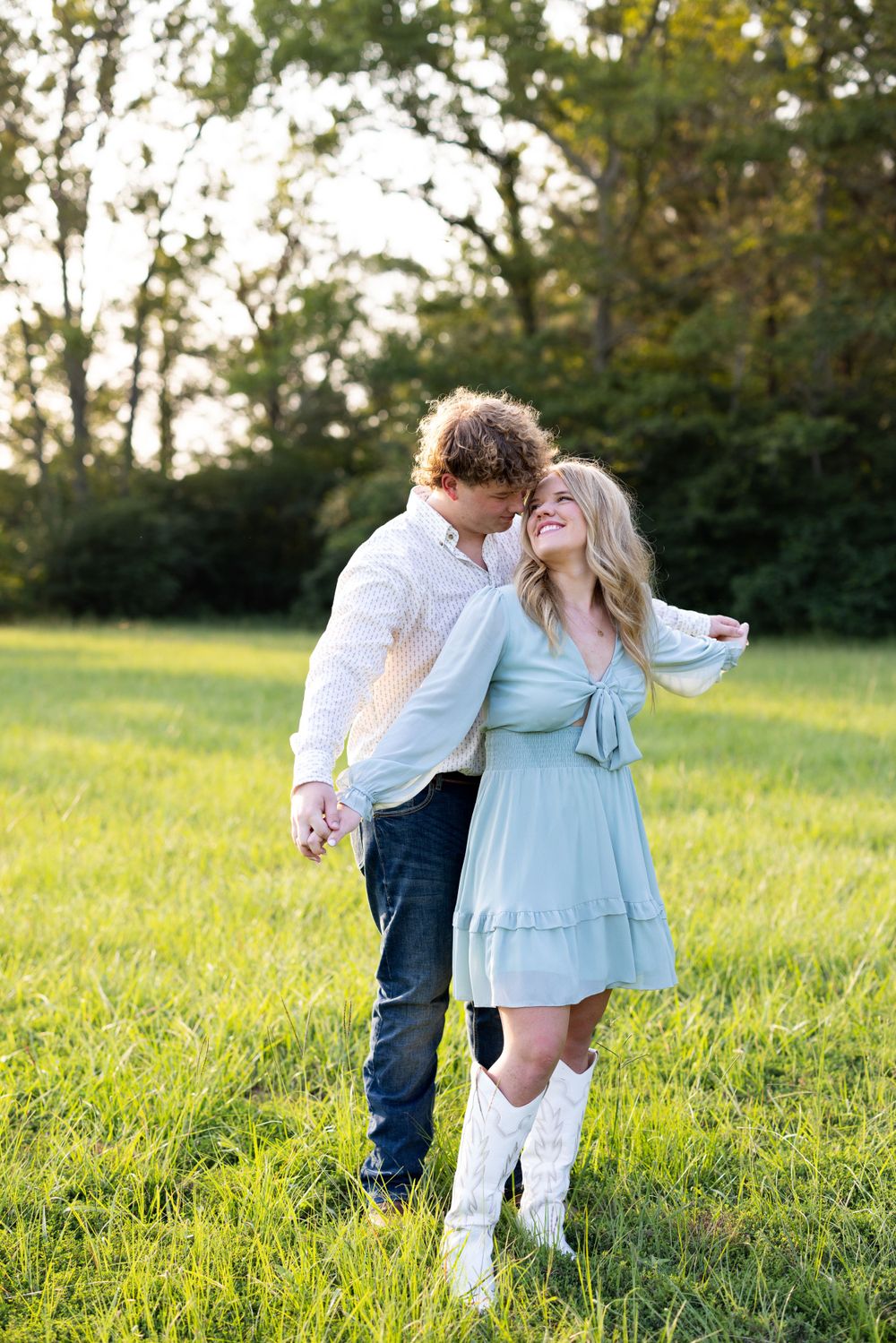 Couple dancing and embracing in a green field during sunset.