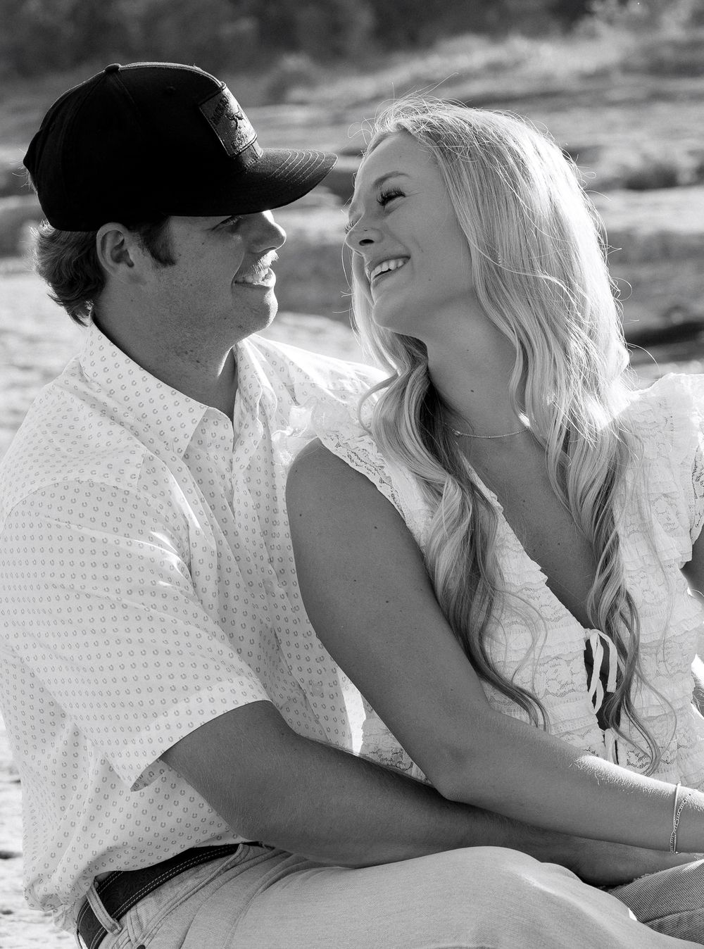 Black and white photo of couple laughing together on beach in casual attire.
