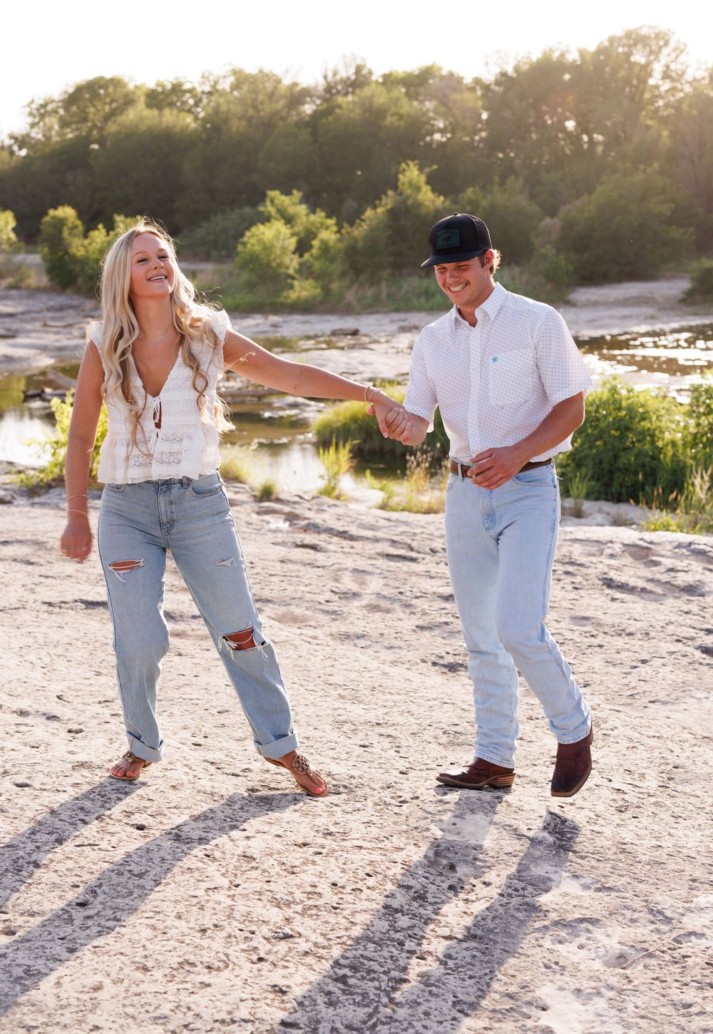 Couple playing and dancing on rocky beach terrain at golden hour.