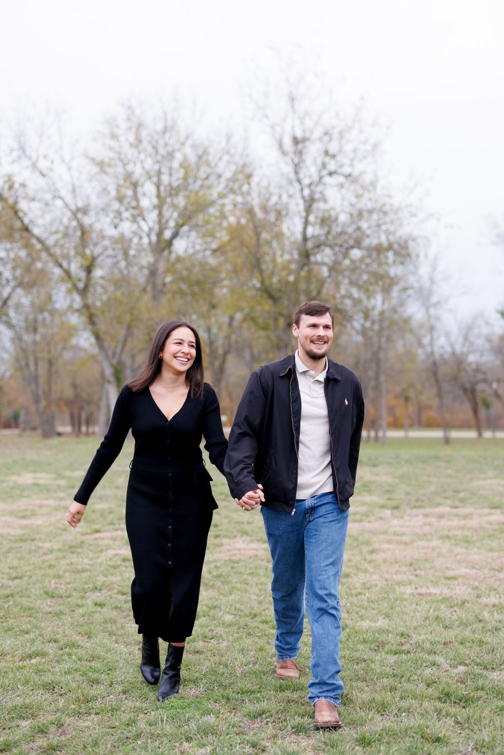 Couple playfully running and holding hands in a grassy field during autumn.