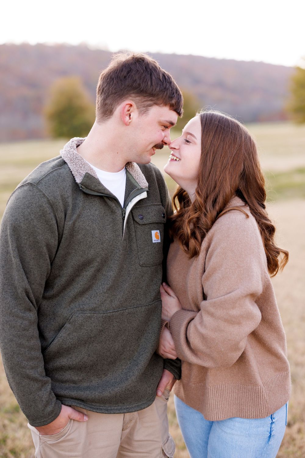 A couple shares playful moments during their engagement photoshoot in a fall field.