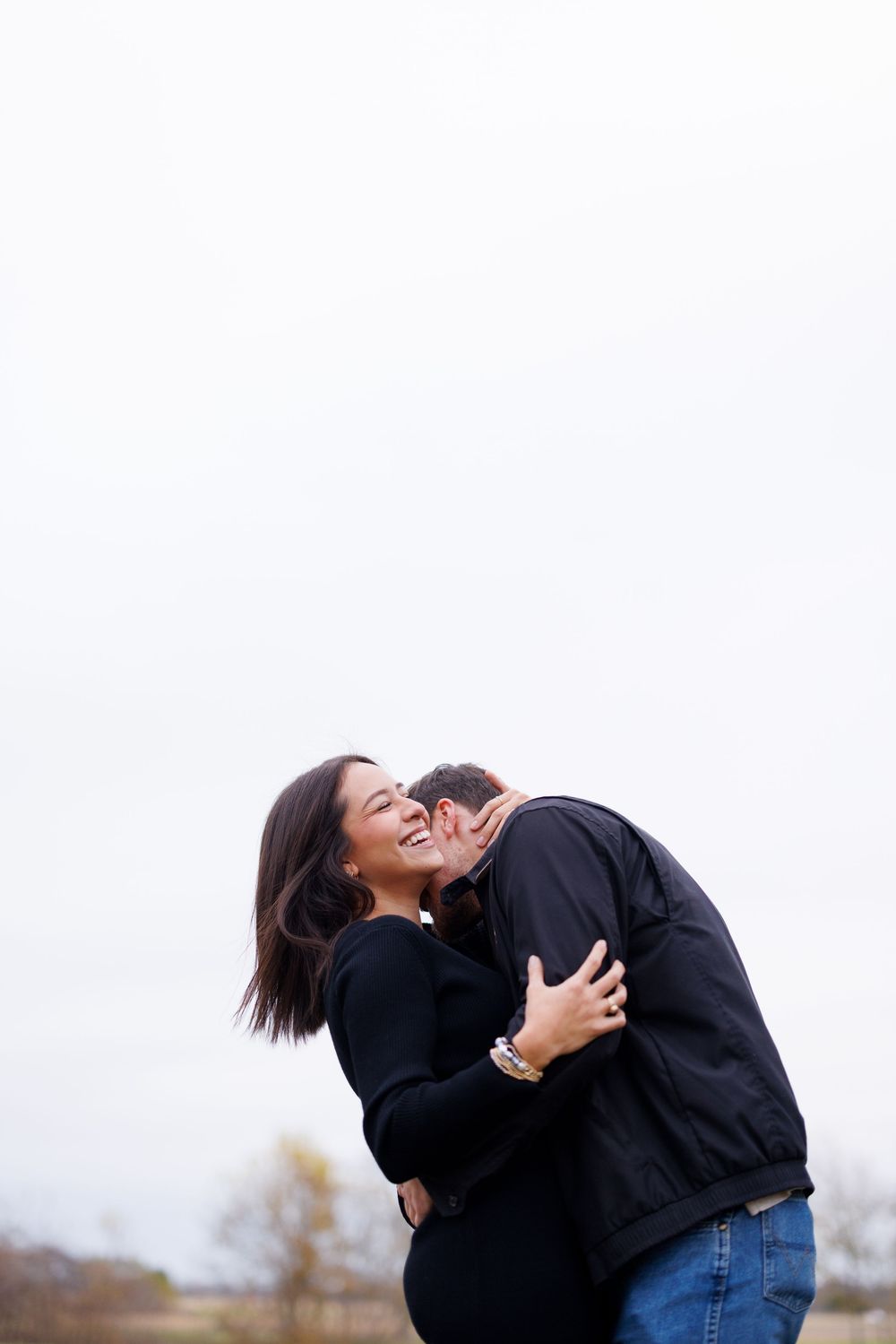 Couple sharing a joyful embrace against overcast sky.