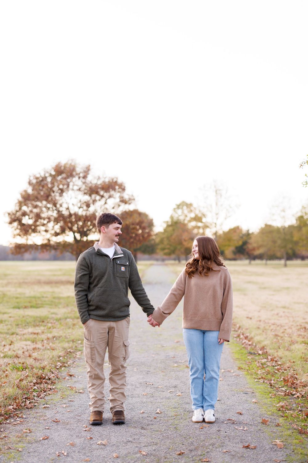 A couple holds hands while walking on a path during an autumn photoshoot.