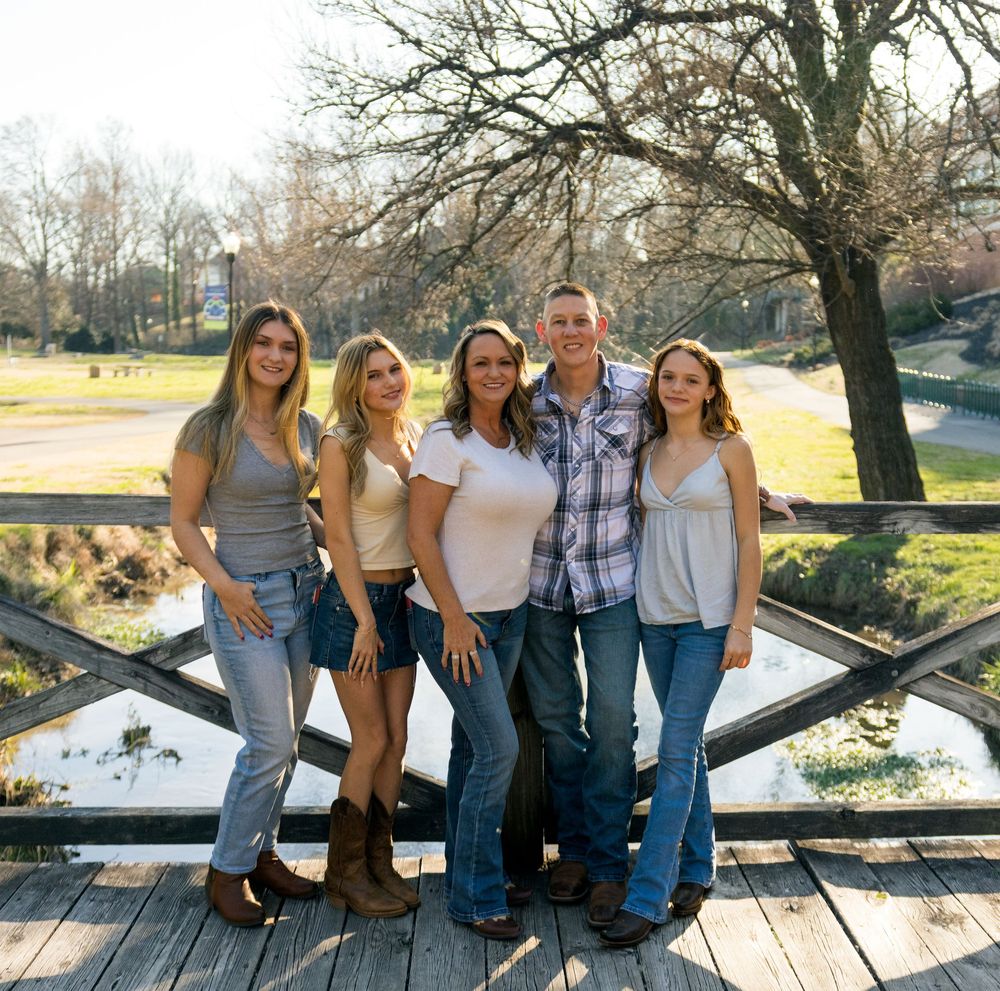 Group of friends posing together on a rustic wooden bridge over water during a sunny outdoor photoshoot.