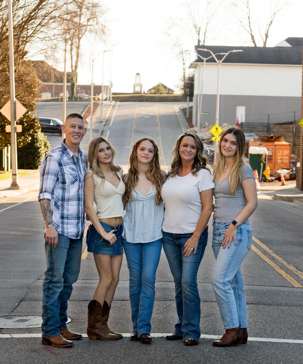 A group of people in casual denim and western wear pose together outdoors at sunset.