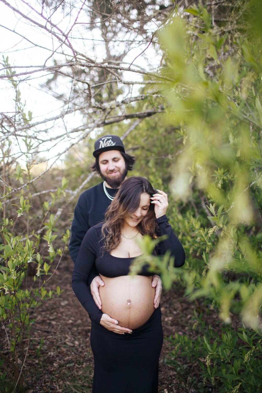 Bothell Maternity Photographer: A couple stand close to each other in a pose during a maternity session outdoors. the woman's belly is bare