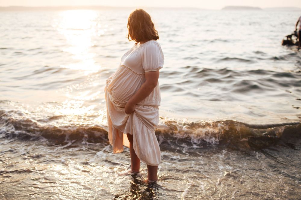 Everett WA Maternity photos: A mom-to-be stands in the water at Howarth Park in Everett at a maternity photo shoot during sunset