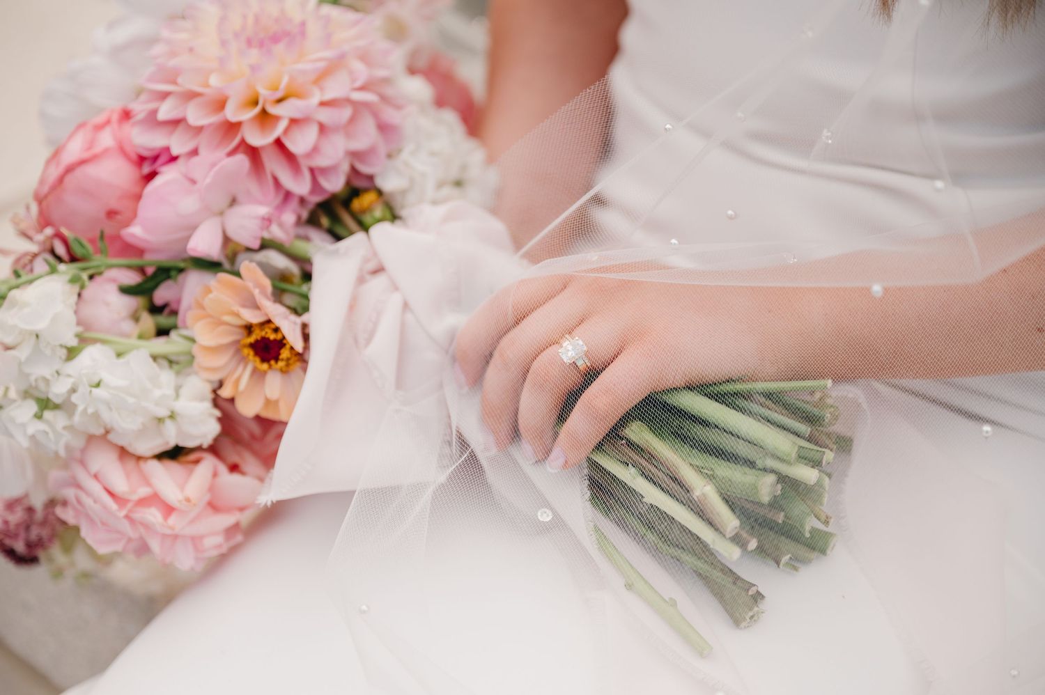 Close-up of hands holding a beautiful pink and white wedding bouquet wrapped in delicate ribbon.