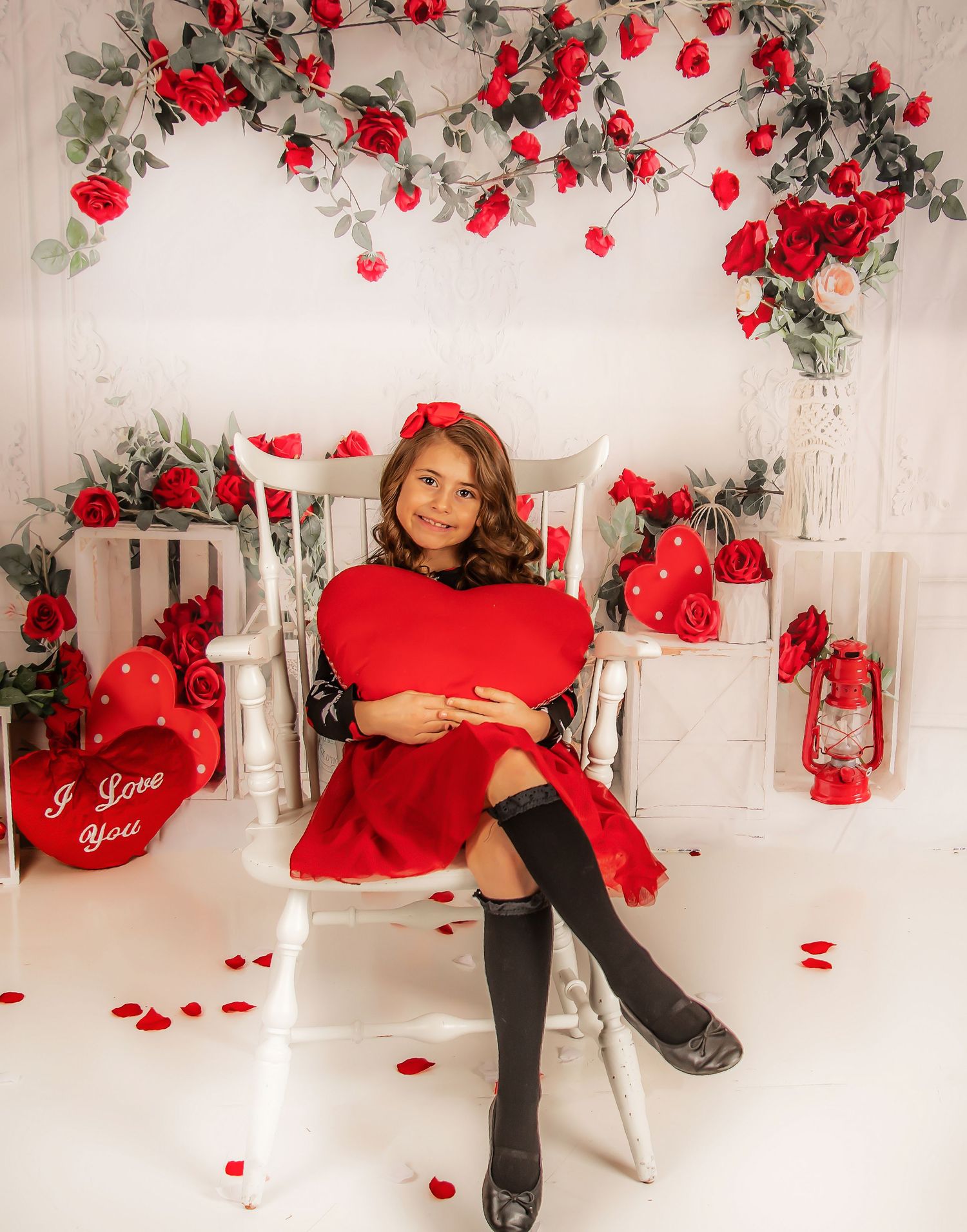 Romantic Valentine's day photo studio setup with red roses, white backdrop, and scattered rose petals on the floor.