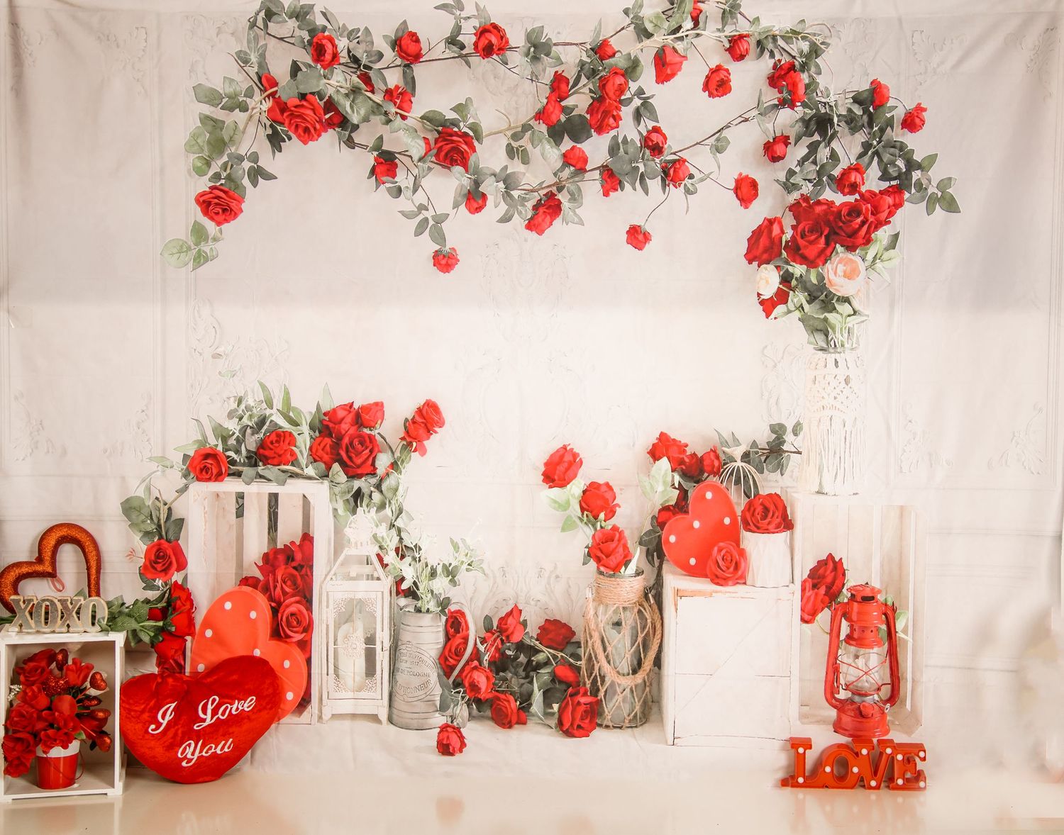 Romantic Valentine's day backdrop with red roses, lanterns and heart decorations against white fabric background.