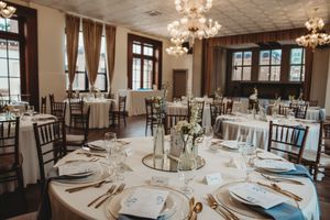 Elegant wedding reception hall with round tables, white linens, gold cutlery, floral centerpieces, and crystal chandeliers.