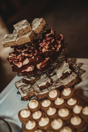 Tiered dessert display with brownies, swirl pastries, and frosted mini cupcakes at a celebration.