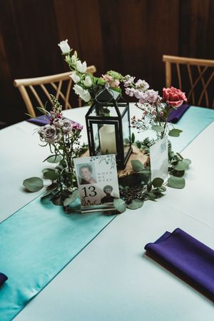Wedding reception table 13 centerpiece featuring black lantern, mixed flowers, eucalyptus, and teal table runner.